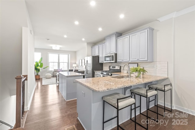 kitchen featuring a kitchen bar, sink, appliances with stainless steel finishes, kitchen peninsula, and light stone countertops