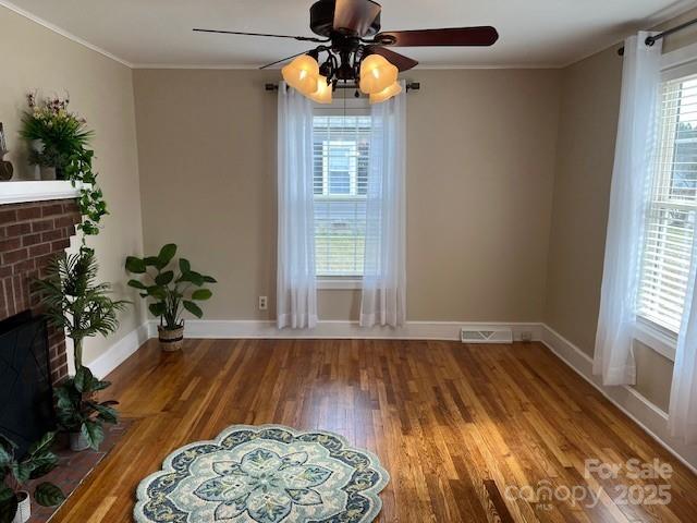 unfurnished room with crown molding, ceiling fan, a brick fireplace, and hardwood / wood-style flooring