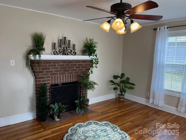 living area featuring hardwood / wood-style flooring, ceiling fan, crown molding, and a brick fireplace