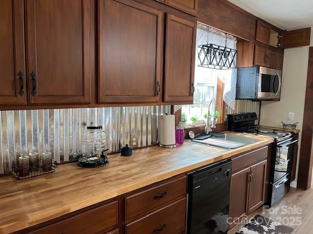 kitchen with light wood-type flooring, wood counters, sink, and black appliances