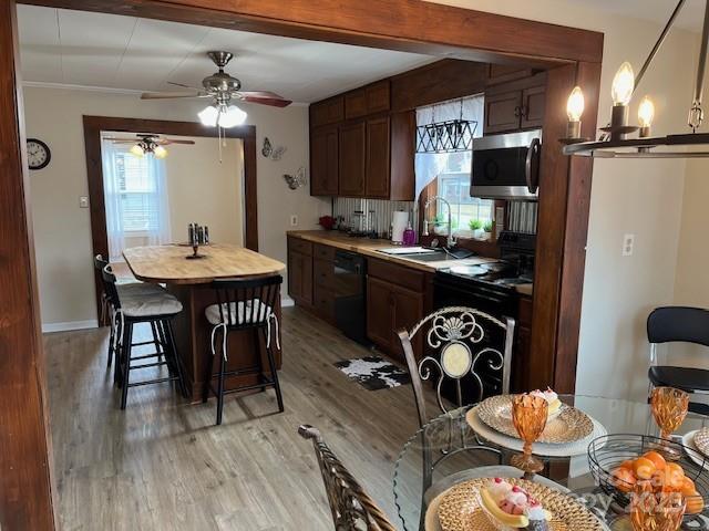 kitchen with sink, a breakfast bar area, light wood-type flooring, black dishwasher, and stove