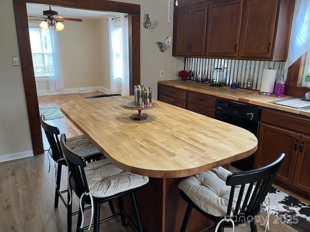 kitchen with wood counters, light hardwood / wood-style flooring, a kitchen breakfast bar, and black dishwasher