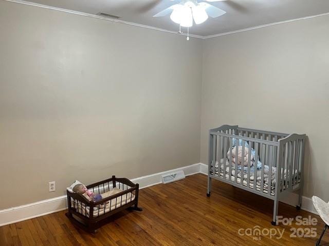 bedroom with crown molding, ceiling fan, dark hardwood / wood-style flooring, and a crib