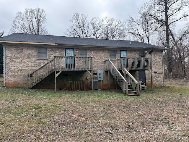 rear view of house with brick siding, a yard, a wooden deck, and stairs