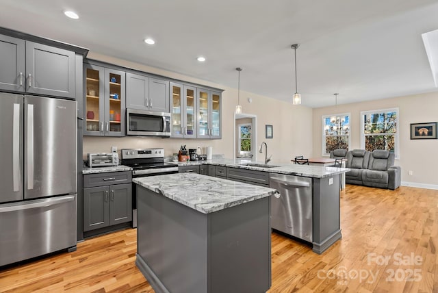 kitchen with gray cabinetry, hanging light fixtures, stainless steel appliances, light stone countertops, and kitchen peninsula