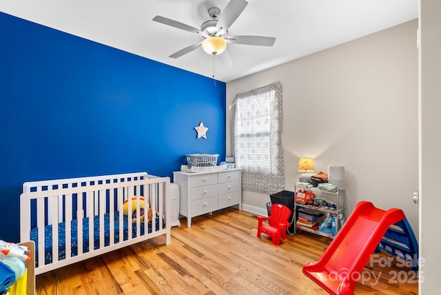 bedroom featuring a crib, ceiling fan, and light hardwood / wood-style flooring
