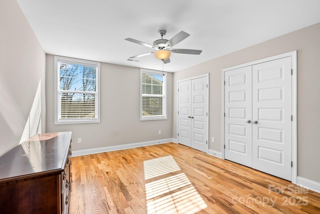 unfurnished bedroom with ceiling fan, light wood-type flooring, and two closets