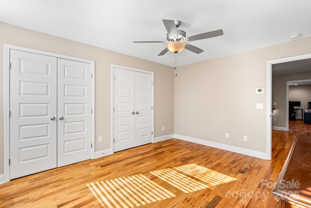 unfurnished bedroom featuring multiple closets, ceiling fan, and wood-type flooring