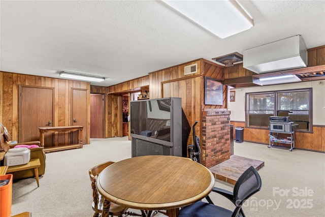 dining room with light carpet, a textured ceiling, and wooden walls