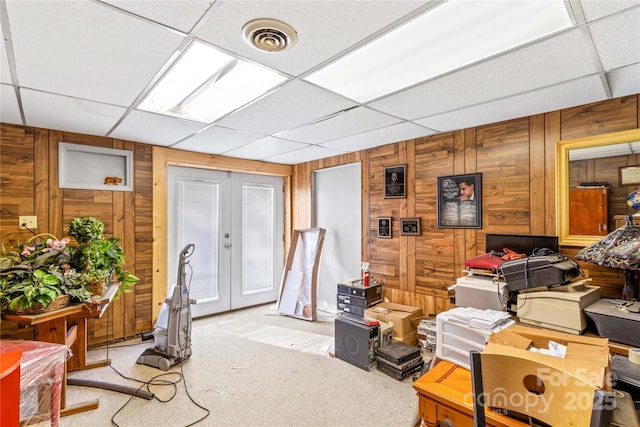 carpeted home office with french doors, wooden walls, and a drop ceiling