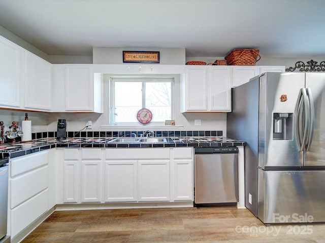 kitchen featuring tile countertops, white cabinetry, sink, light hardwood / wood-style floors, and stainless steel appliances