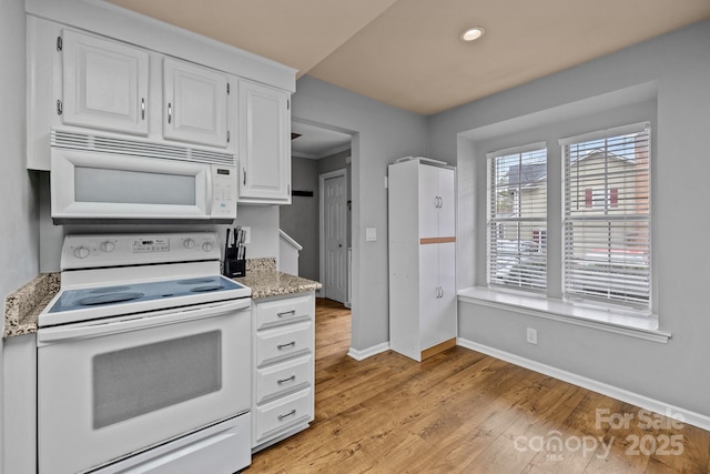 kitchen with white cabinetry, white appliances, light stone countertops, and light hardwood / wood-style floors