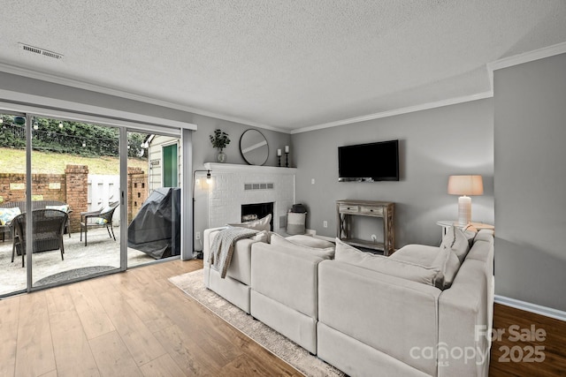 living room featuring a textured ceiling, ornamental molding, a brick fireplace, and light hardwood / wood-style floors