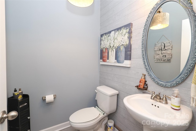 bathroom with sink, wooden walls, and toilet