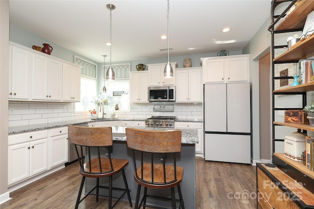 kitchen with dark stone countertops, hanging light fixtures, stainless steel appliances, a center island, and white cabinets