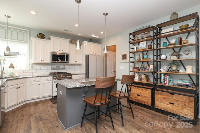 kitchen with appliances with stainless steel finishes, white cabinets, light stone counters, and decorative light fixtures