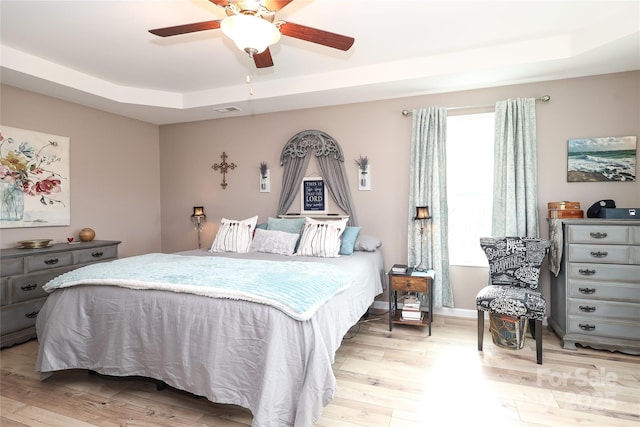 bedroom with ceiling fan, light hardwood / wood-style floors, and a tray ceiling