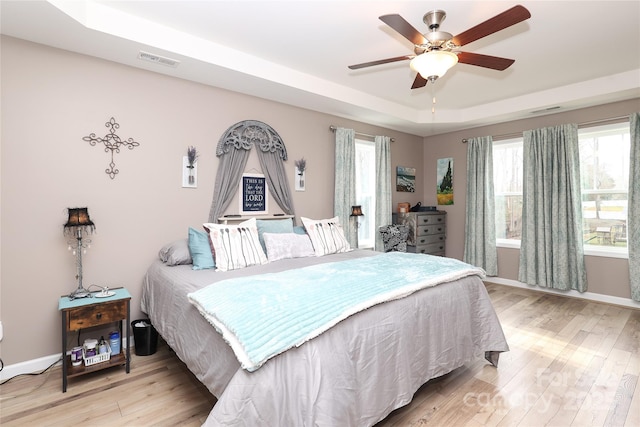 bedroom with multiple windows, a tray ceiling, and light wood-type flooring