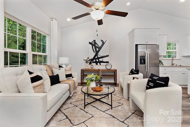 living room featuring ceiling fan, lofted ceiling, sink, and light hardwood / wood-style flooring