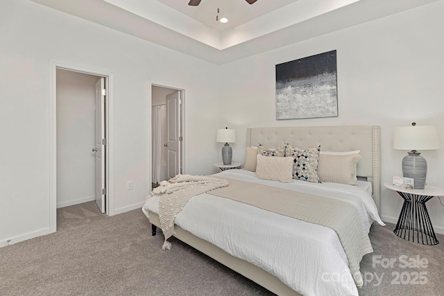 bedroom with a raised ceiling, ensuite bathroom, carpet floors, and ceiling fan