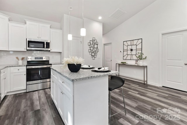 kitchen with decorative light fixtures, appliances with stainless steel finishes, a kitchen breakfast bar, light stone countertops, and white cabinets