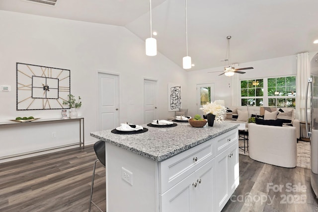 kitchen with dark hardwood / wood-style floors, decorative light fixtures, white cabinetry, a kitchen bar, and light stone counters