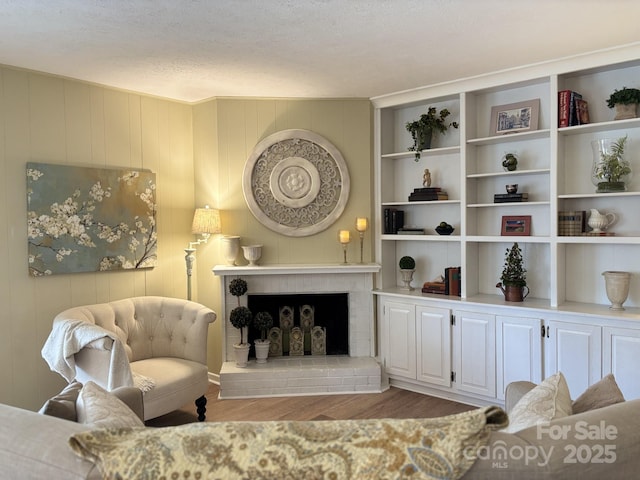 living area featuring hardwood / wood-style flooring, a brick fireplace, and a textured ceiling