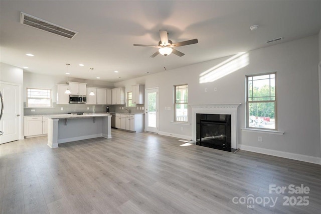 unfurnished living room with a healthy amount of sunlight, sink, ceiling fan, and light hardwood / wood-style flooring