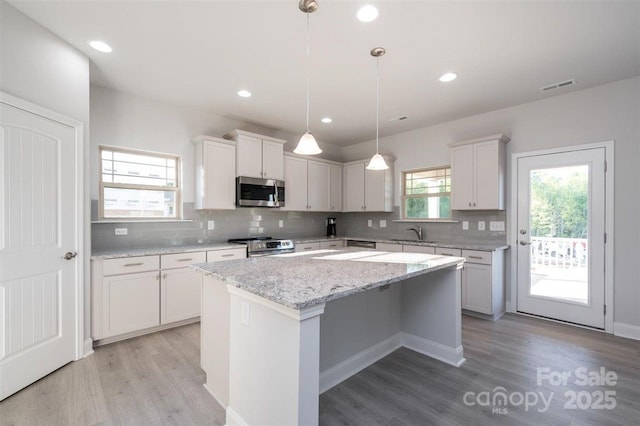 kitchen featuring decorative light fixtures, white cabinetry, sink, a center island, and stainless steel appliances