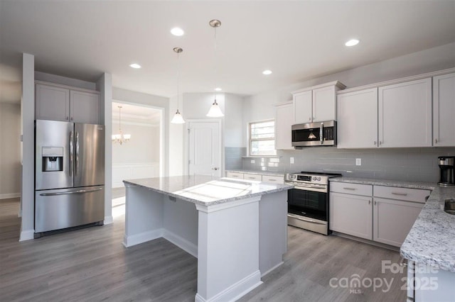 kitchen with stainless steel appliances, light stone countertops, a kitchen island, and hanging light fixtures