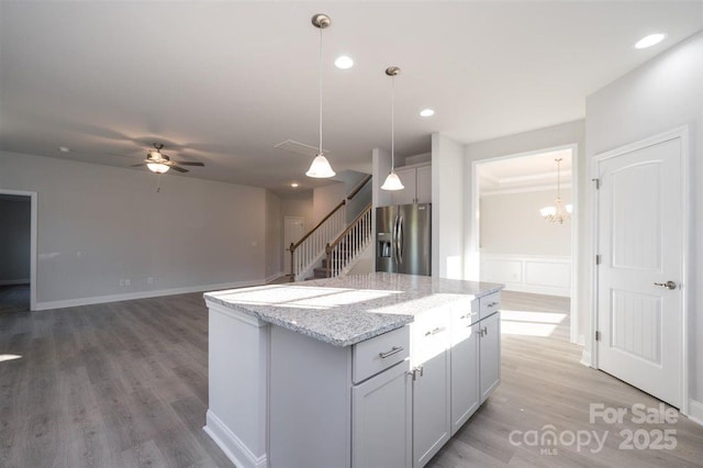 kitchen with stainless steel refrigerator with ice dispenser, a center island, hardwood / wood-style floors, and light stone countertops