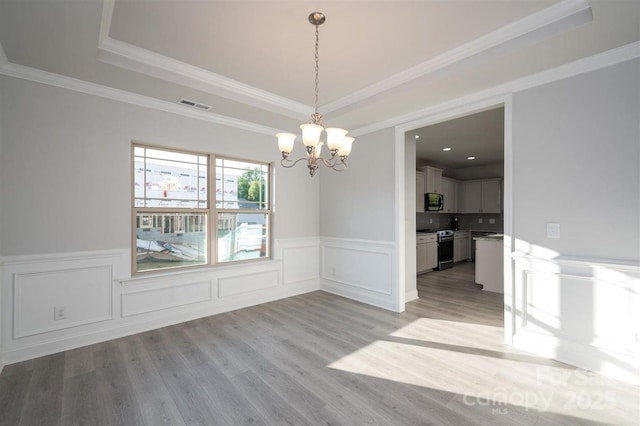 unfurnished dining area with crown molding, a tray ceiling, and light wood-type flooring