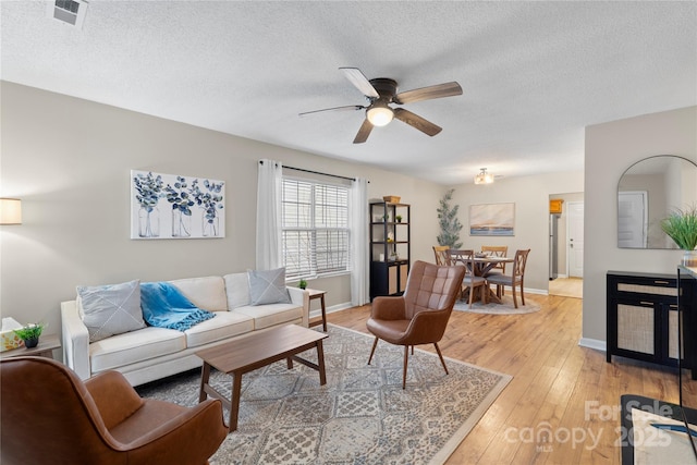 living room featuring ceiling fan, hardwood / wood-style flooring, and a textured ceiling