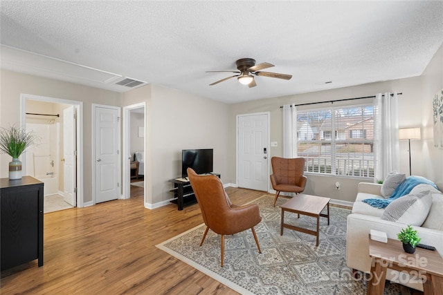 living room featuring ceiling fan, light hardwood / wood-style flooring, and a textured ceiling