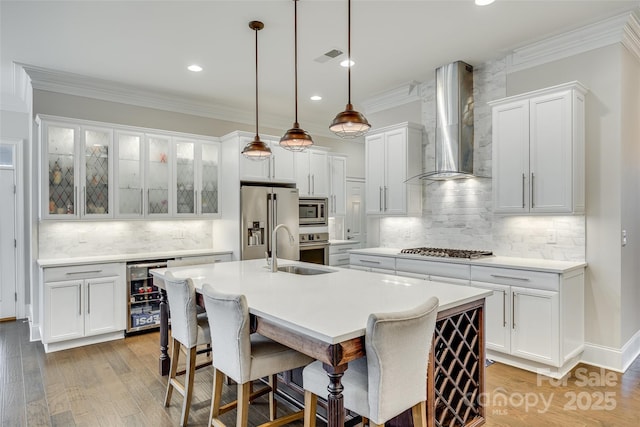 kitchen with white cabinetry, a center island with sink, stainless steel appliances, beverage cooler, and wall chimney range hood