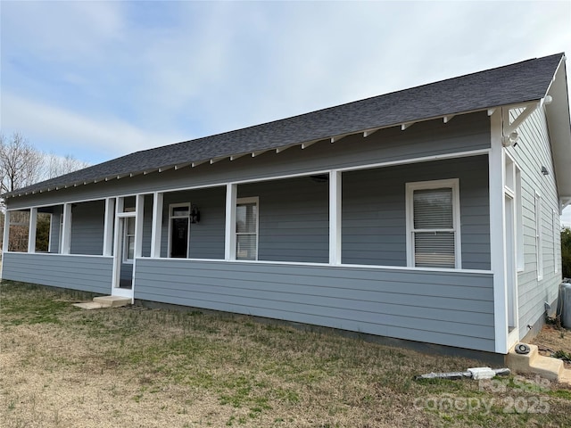 view of side of home with a porch, roof with shingles, and a lawn