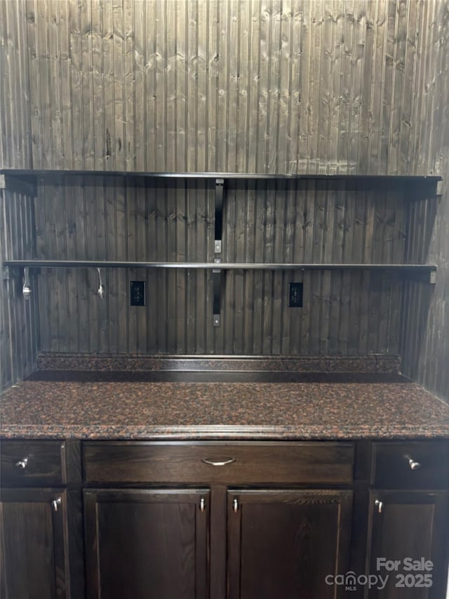 bar with dark brown cabinetry and dark stone counters