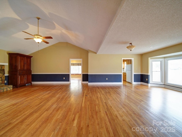 unfurnished living room featuring ceiling fan, vaulted ceiling, a textured ceiling, and light wood-type flooring