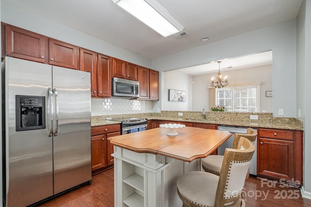 kitchen with pendant lighting, a kitchen breakfast bar, stainless steel appliances, light stone countertops, and kitchen peninsula