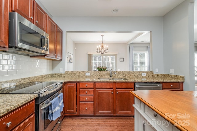 kitchen featuring sink, backsplash, stainless steel appliances, light stone counters, and light hardwood / wood-style floors