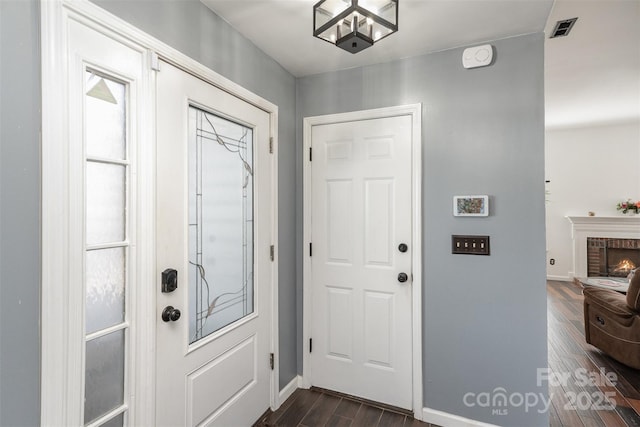 foyer entrance with dark wood-type flooring and a brick fireplace