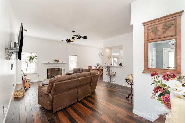 living room with a brick fireplace, dark wood-type flooring, and ceiling fan