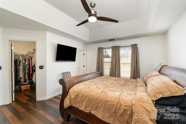 bedroom with dark wood-type flooring, ceiling fan, a raised ceiling, a spacious closet, and a closet