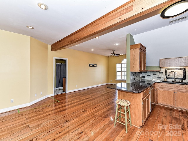 kitchen with beamed ceiling, tasteful backsplash, dark stone countertops, a kitchen bar, and kitchen peninsula