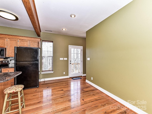 kitchen with stove, light hardwood / wood-style floors, beamed ceiling, and black fridge