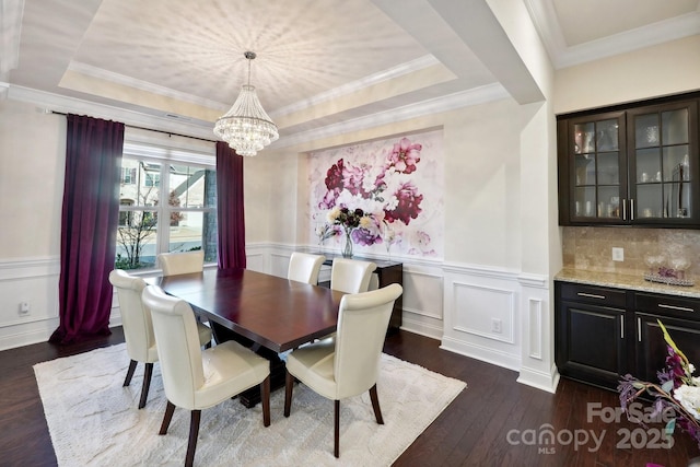 dining room featuring a raised ceiling, ornamental molding, an inviting chandelier, and dark hardwood / wood-style flooring