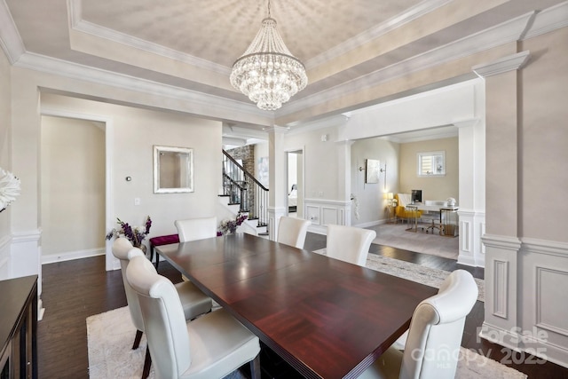 dining space with ornate columns, dark hardwood / wood-style floors, a chandelier, a raised ceiling, and crown molding