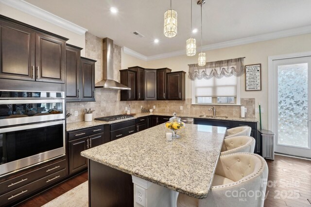 kitchen featuring wall chimney range hood, a breakfast bar, hanging light fixtures, a center island, and decorative backsplash