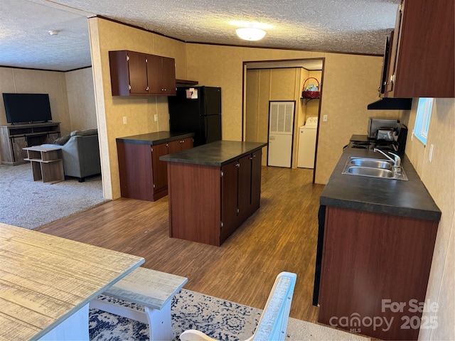 kitchen with sink, dark wood-type flooring, ornamental molding, a kitchen island, and black fridge