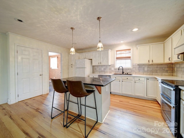 kitchen featuring sink, appliances with stainless steel finishes, white cabinetry, a kitchen island, and light wood-type flooring